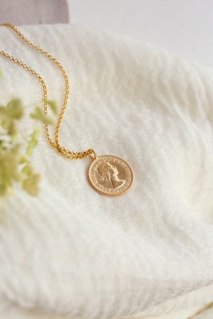 Gold necklace with a coin pendant on a soft white fabric background