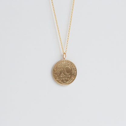 Gold necklace with a round pendant on a light gray background. 50th brithday gift for her with a 1976 French coin pendant. 