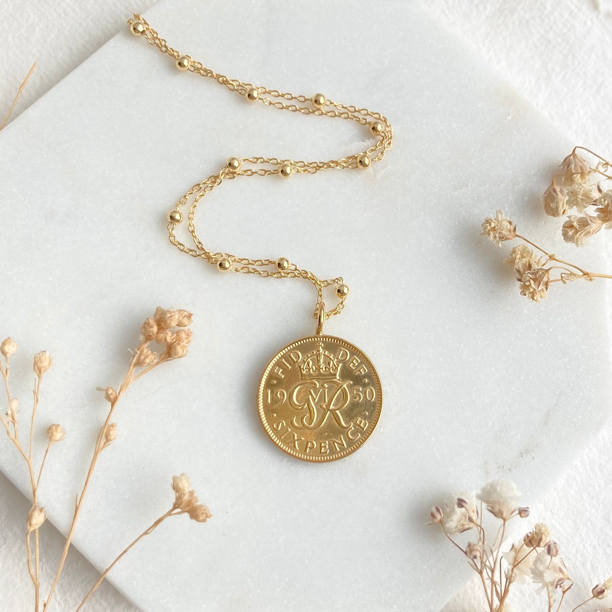 Gold necklace with a round pendant on a white surface with dried flowers.