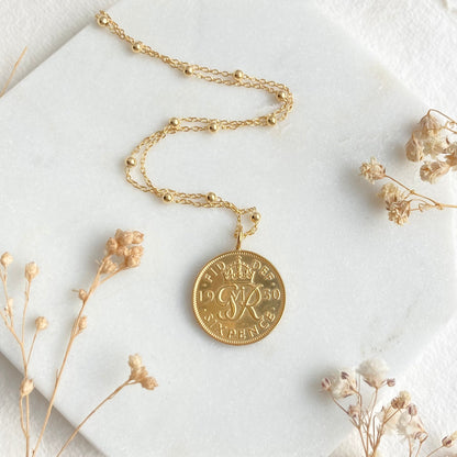 Gold necklace with a round pendant on a white surface with dried flowers.