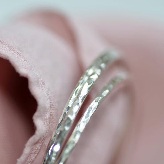 A close up of some of our signature Prenoa bangles with their elegant hammered finish. Sterling silver, held in a linen polishing cloth.