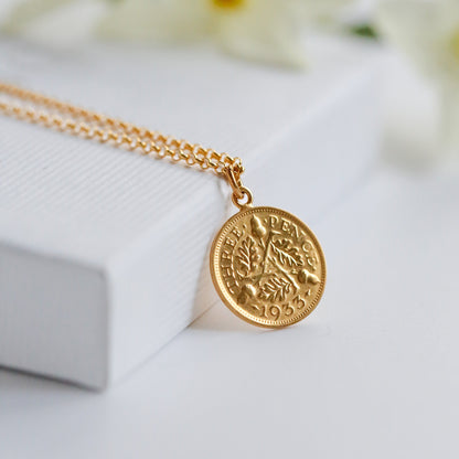 A gold 22carat plated threepence British vintage coin necklace sits on a white box.