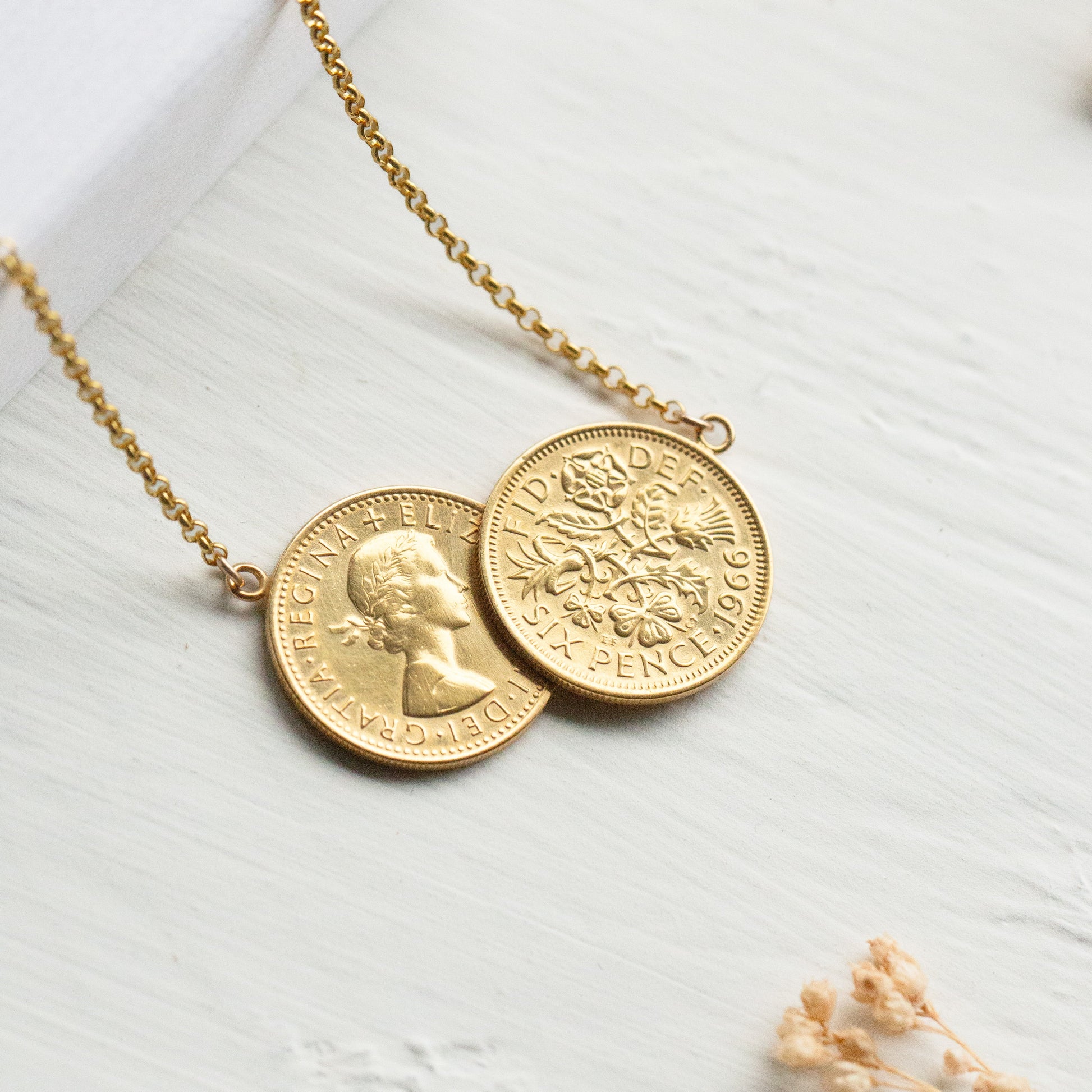 Gold sixpence necklace with two coins on a light wooden surface
