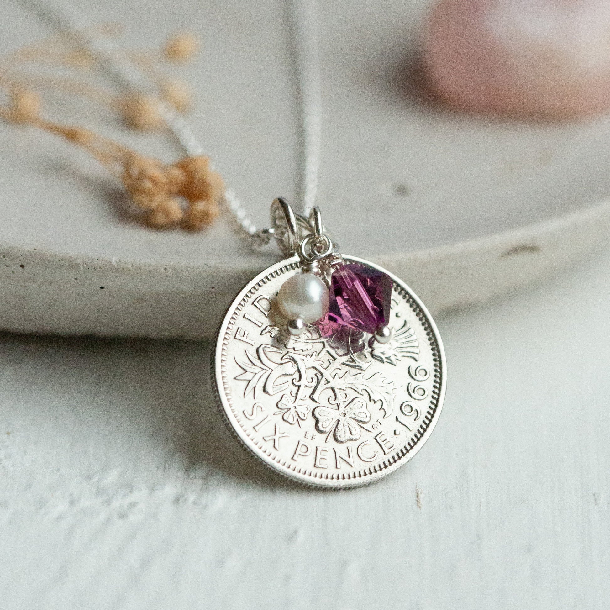 Silver British coin pendant necklace with a purple gemstone on a light background