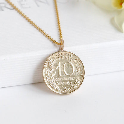Gold coin necklace on a white surface with flowers in the background