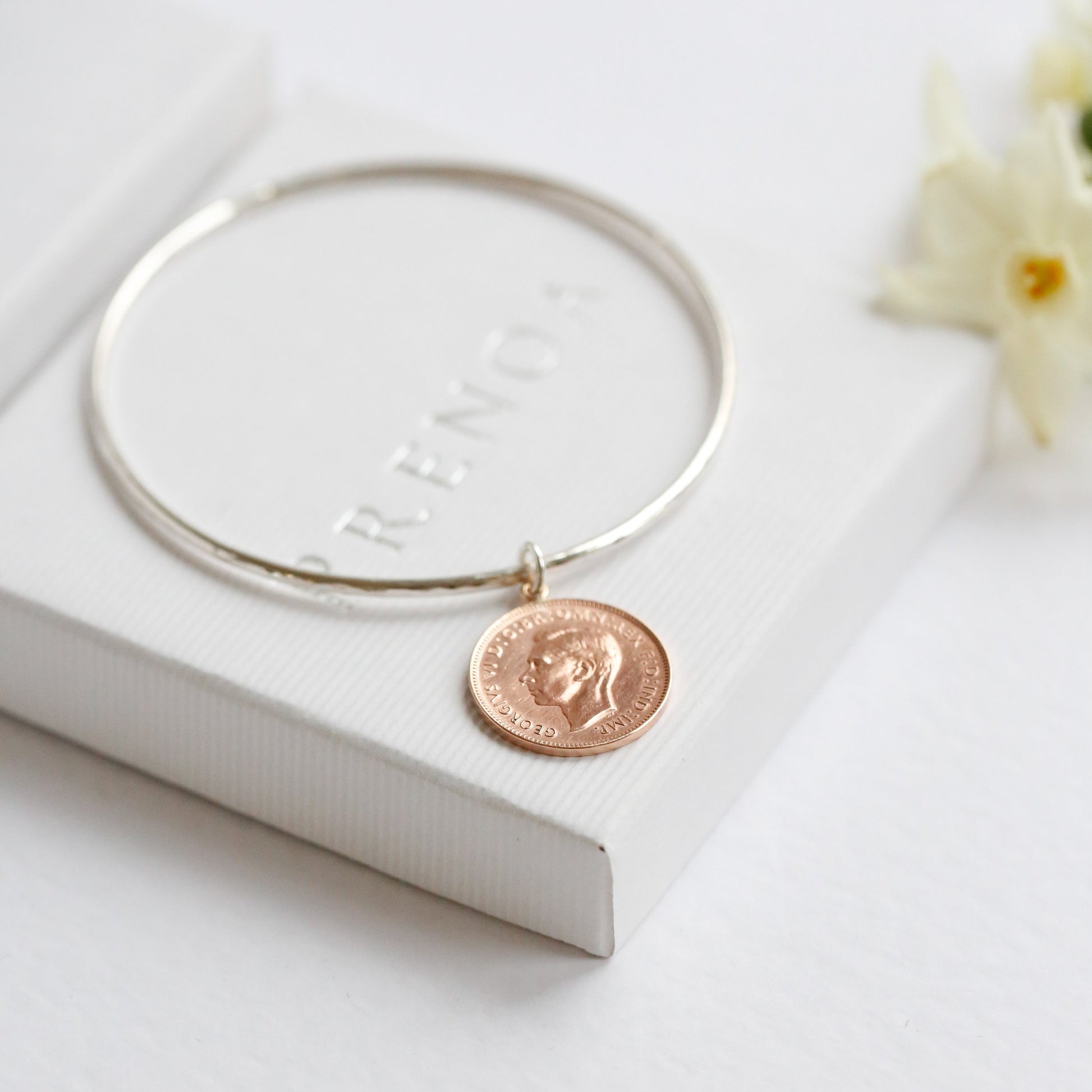 Silver bangle with a bronze coin charm on a white surface