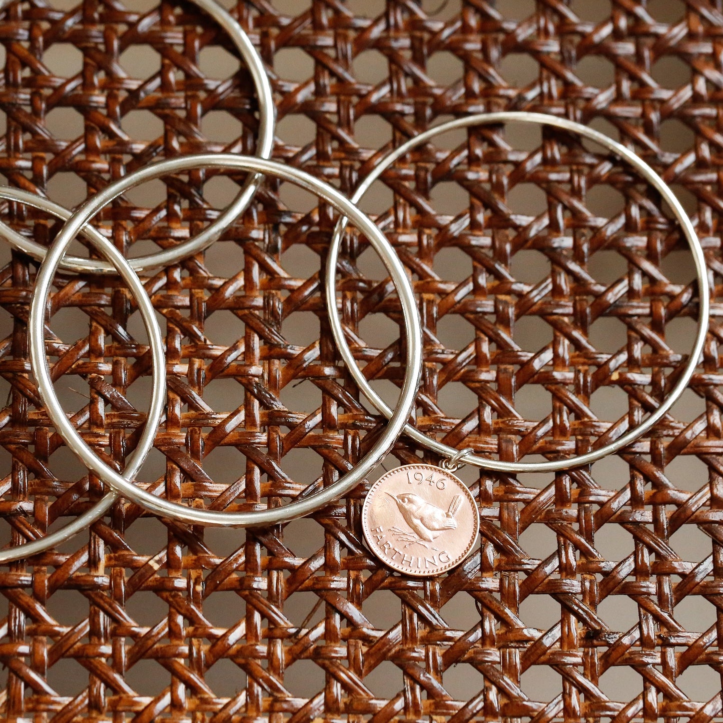 Three silver hoop earrings on a brown woven surface with a penny for scale.