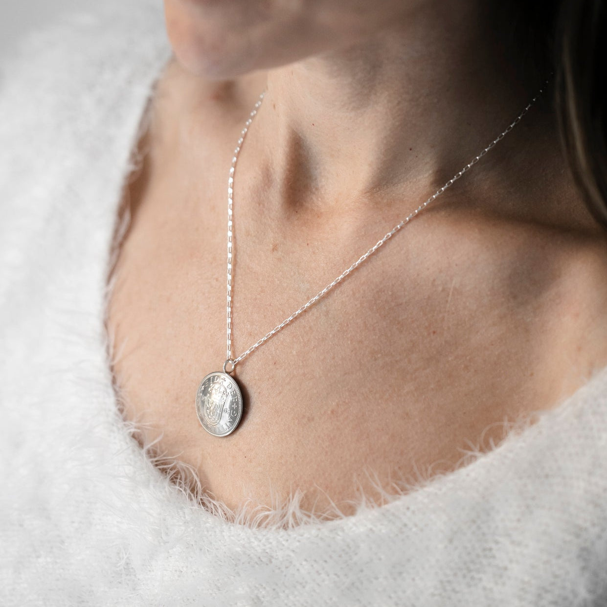 Shilling coin necklace on a sterling silver chain on a female neck wearing a white jumper