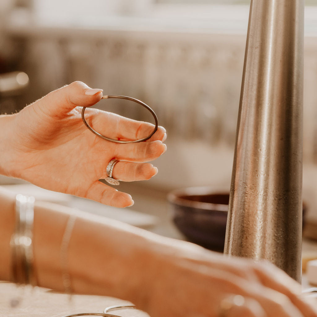 Person holding a sterling silver infinity stacking bangle, with a mandrel in the Prenoa jewellery workshop.