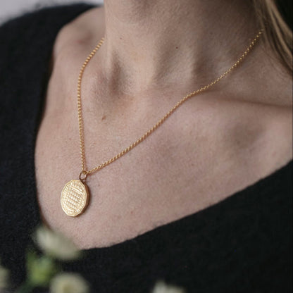 Queen Elizabeth coin pendant with gold vermeil chain sits on the neck of a woman in a navy blue jumper.