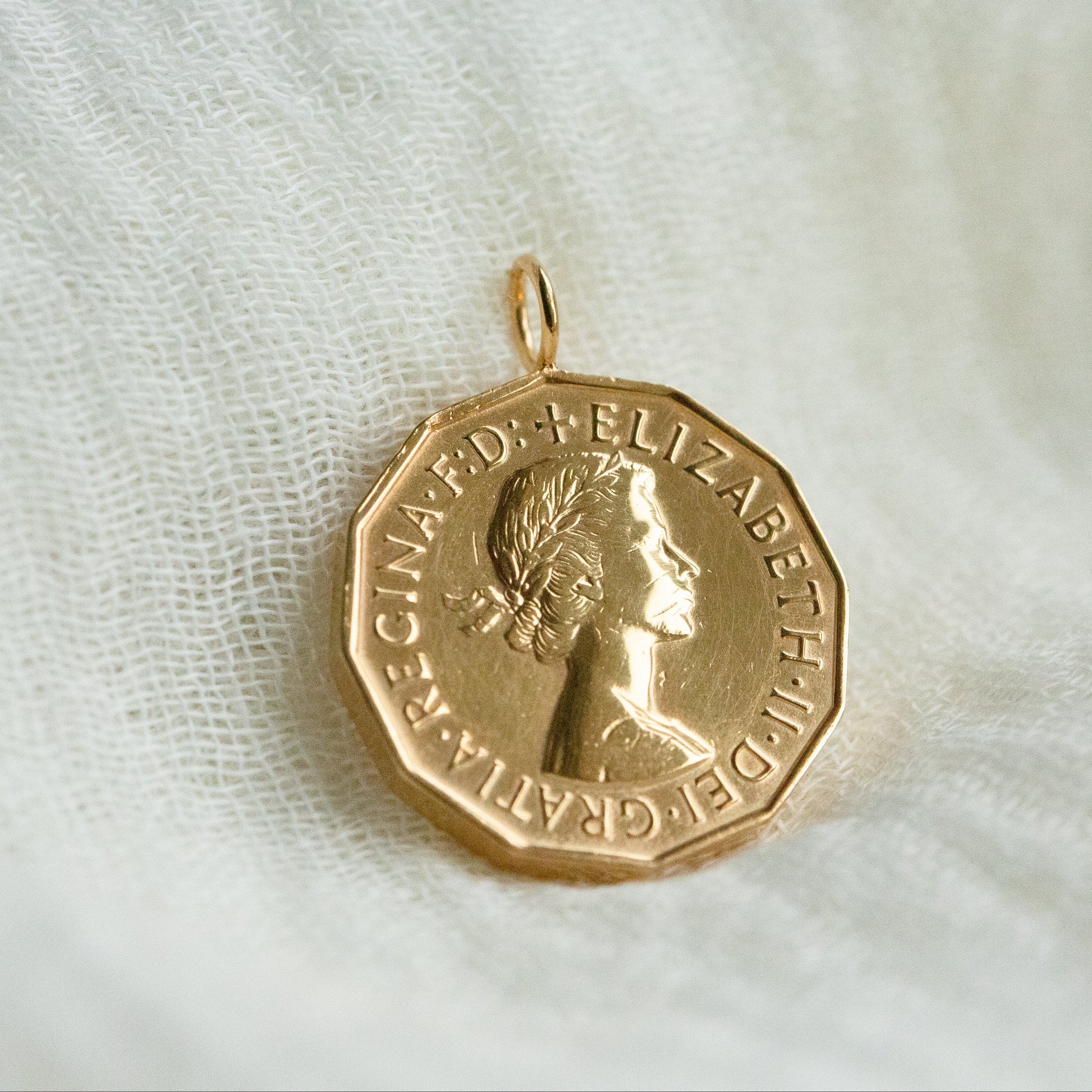 Gold coin pendant with Queen Elizabeth II's portrait on a white fabric background