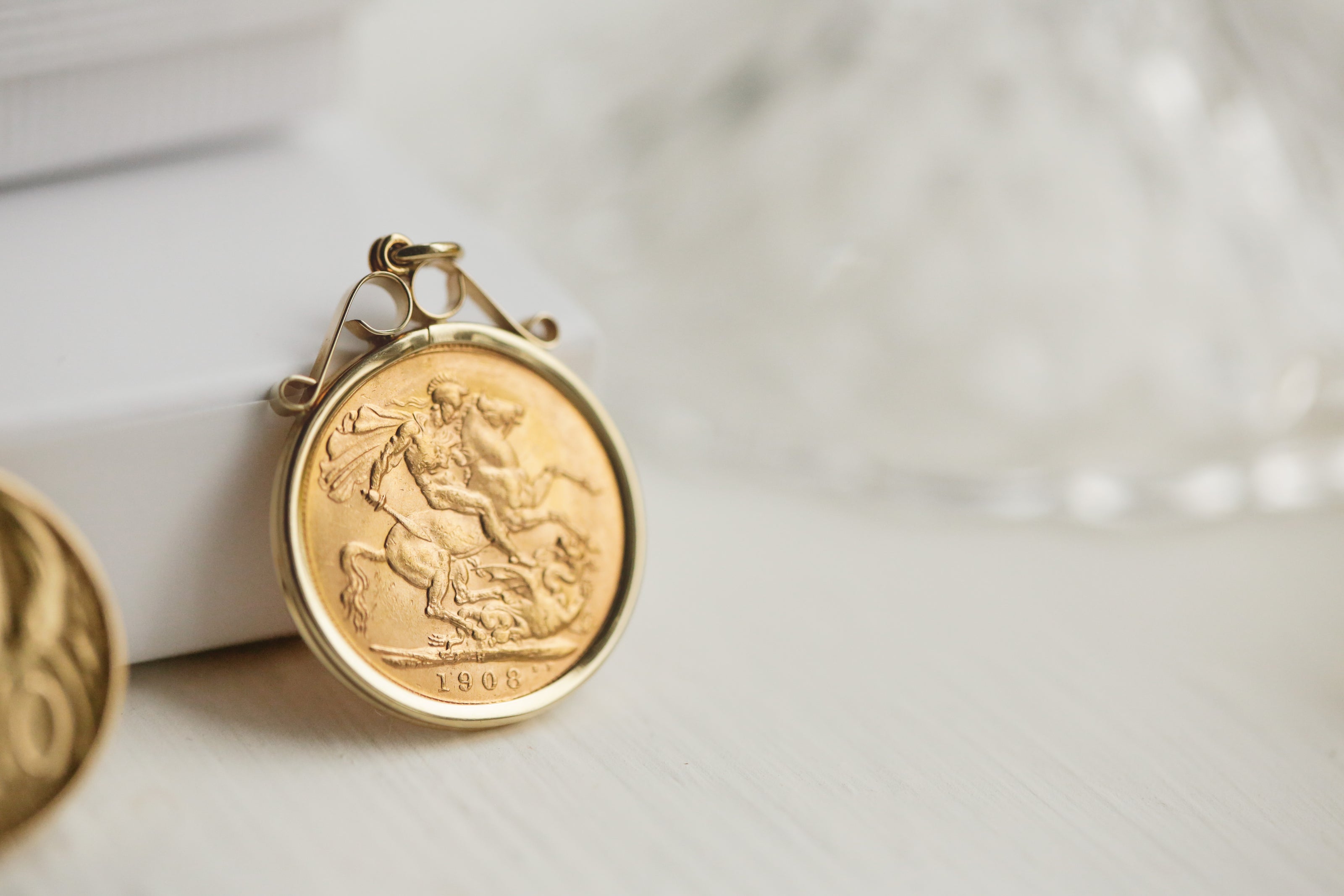 22ct St George and the dragon sovereign Gold coin pendant in a 9ct gold scroll mount bezel design, laid on a white background