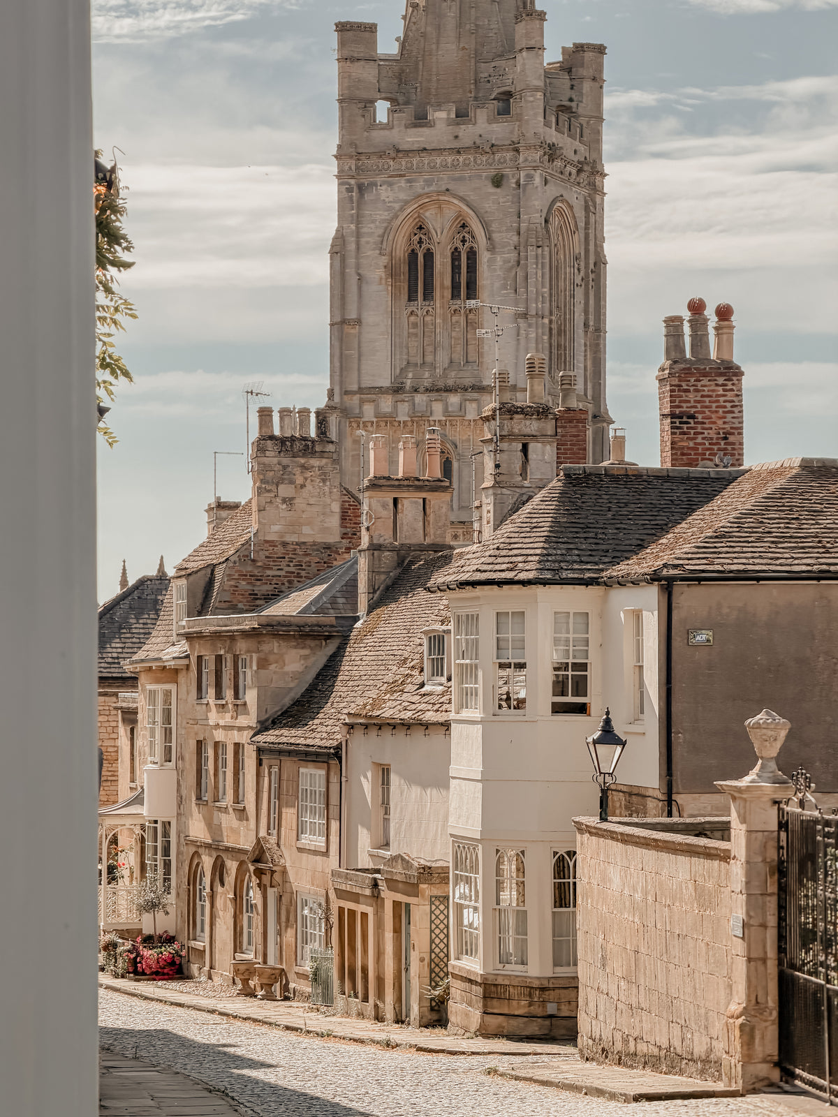 A scenic view of the historic street  Barn Hill in Stamford UK with old stone buildings, dark tiled roofs, and the tower of All Saints' Church rising in the background under a cloudy sky. - copyright of and credit to theoldbuilding