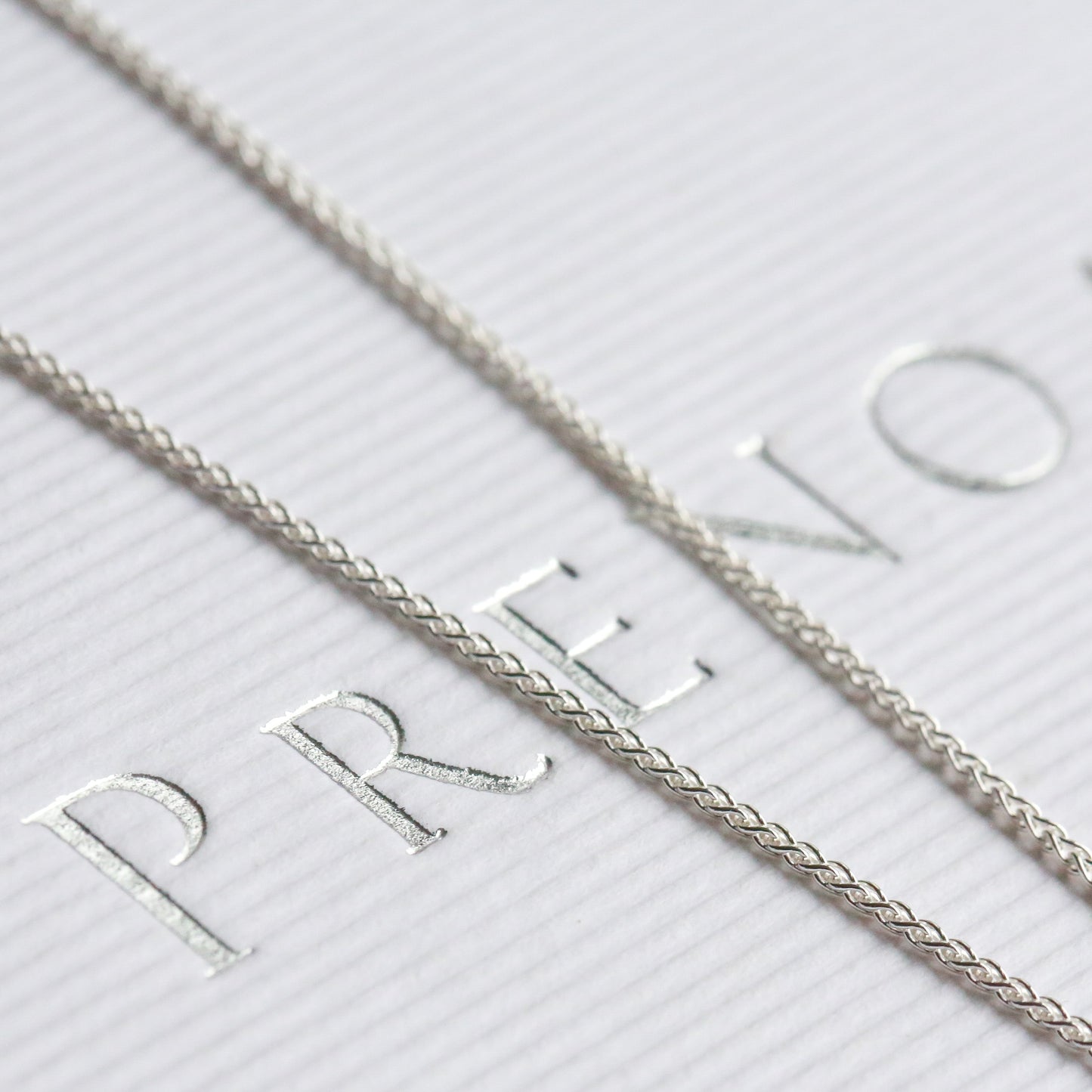 Silver necklace on a white box with 'PRENOA' branding.