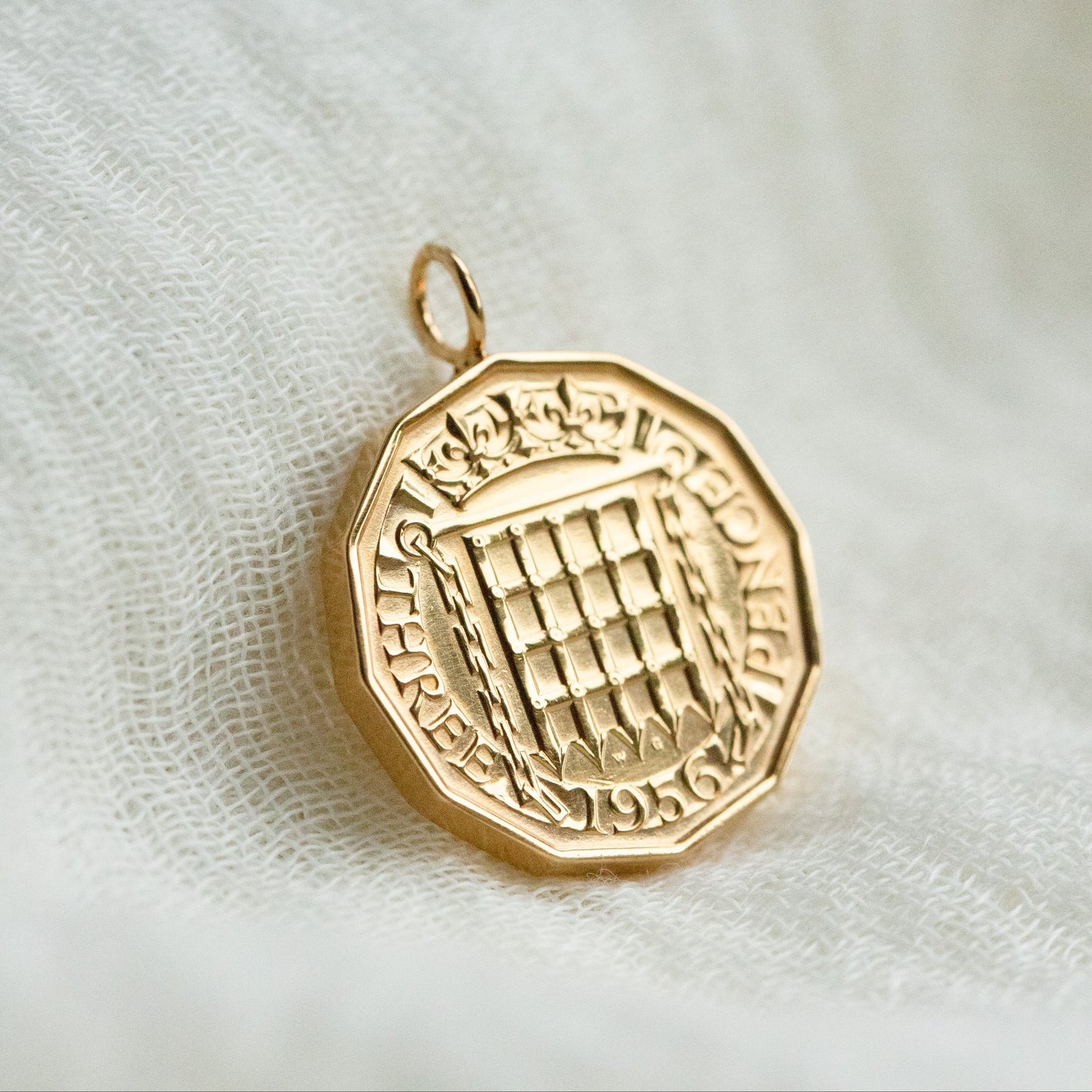 A real British threepence coin with a solid gold bail, sits on a fabric background