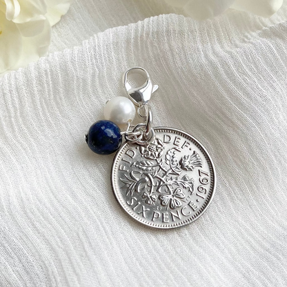 Something old, something new, something borrowed and something blue wedding charm, made with a British sixpence coin and silver findings. The charm of lapis blue lazuli and a freshwater pearl sit next to the coin and hang from a lobster claw clasp, ideal for fixing to a bouquet or garter.