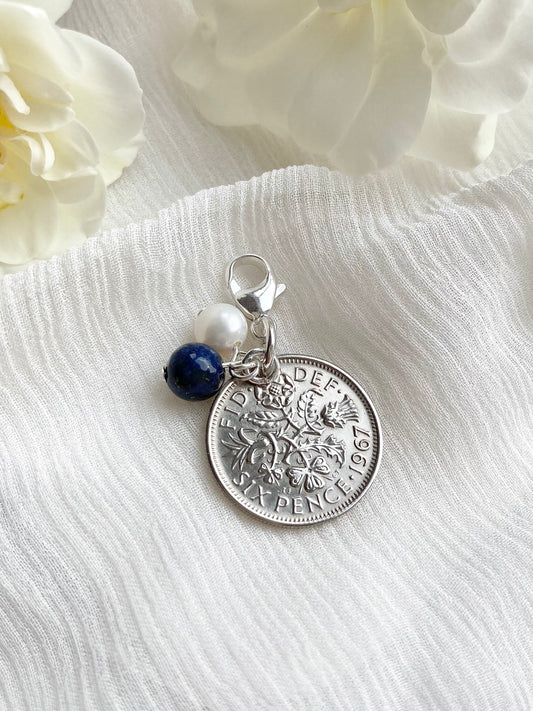 Something old, something new, something borrowed and something blue wedding charm, made with a British sixpence coin and silver findings. The charm of lapis blue lazuli and a freshwater pearl sit next to the coin and hang from a lobster claw clasp, ideal for fixing to a bouquet or garter.
