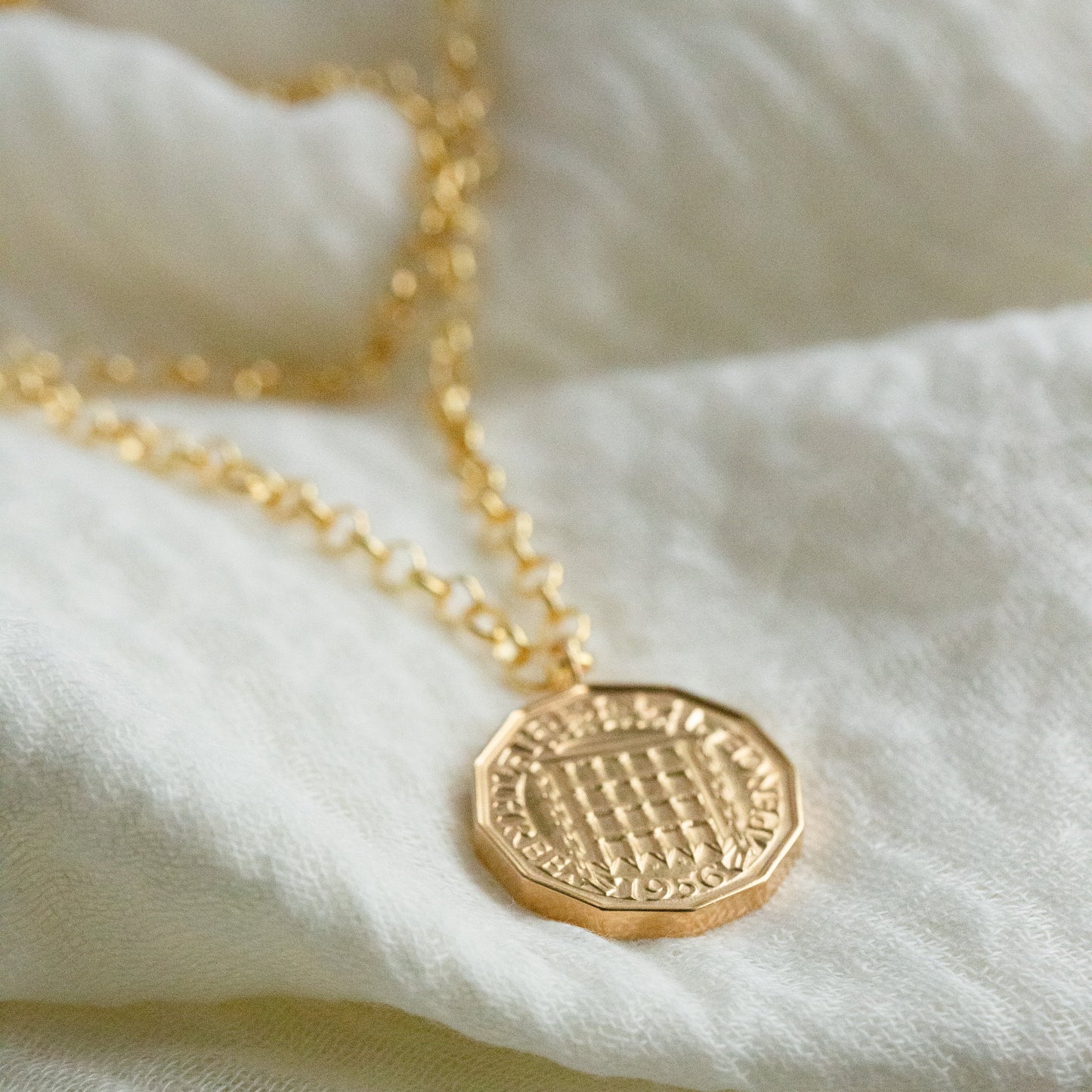 Gold necklace with a textured pendant on a white fabric background
