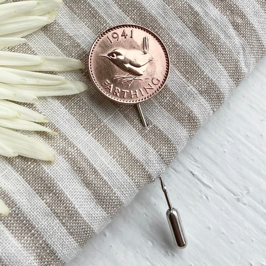 A bronze-colored lapel pin with a bird design, placed on a striped fabric.