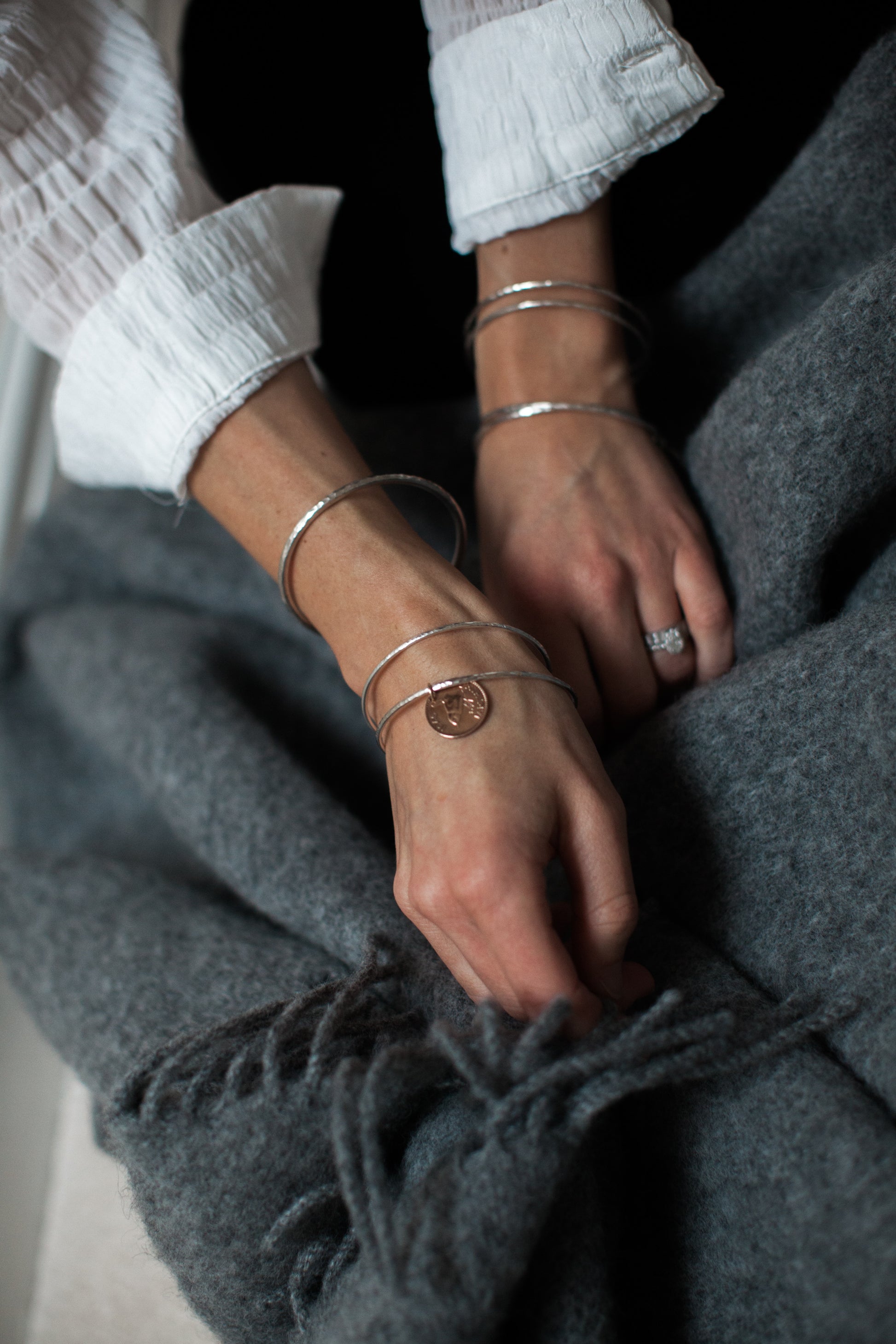 Modelled sterling silver hammered infinity bangles. Model wears a white shirt and folds a dark grey woolen blanket.