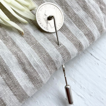 A silver coin lapel pin on a striped linen cloth with white background and suggestion of a flower in the top left.