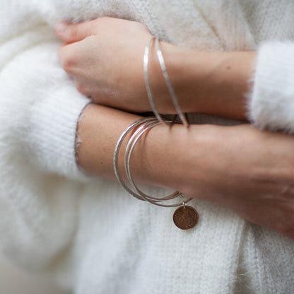 Sterling silver coin bangles with farthing coins, shown on a wrist with white jumper.