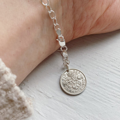 A sterling silver bracelet featuring an oval link chain and a British sixpence coin charm, displayed on a person's wrist.