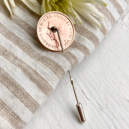 Farthing coin in bronze with a lapel pin sterling silver back, sitting on linen fabric. Coin accessories by Prenoa. 